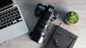 A computer, camera, and a notebook on a desk