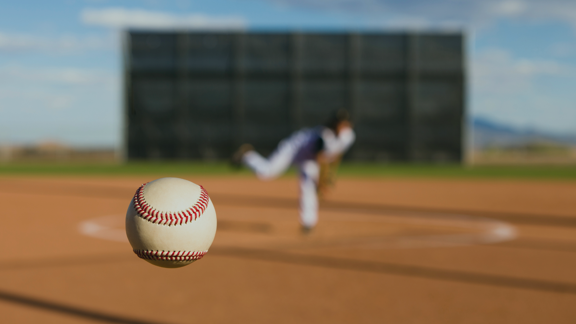 A blurry pitcher in the background on a baseball field with a clear baseball in the foreground.